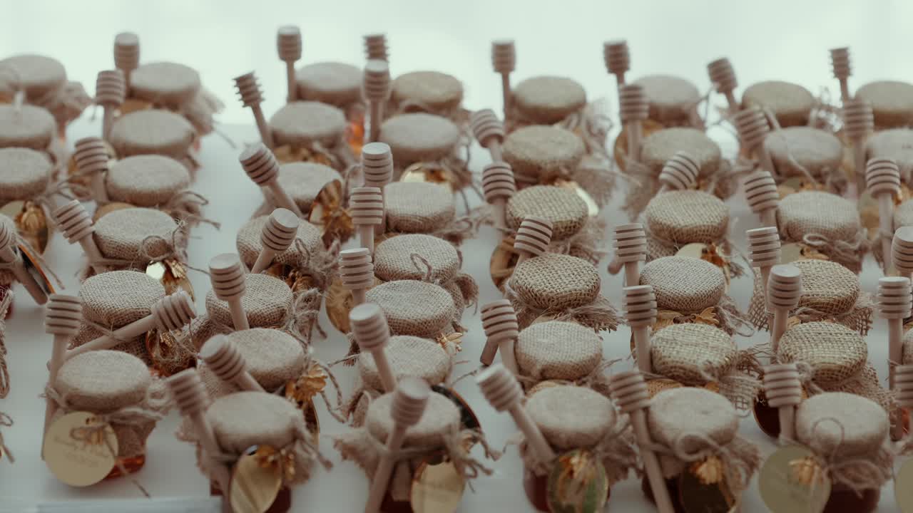 small glass jars of honey with burlap covers and wooden dippers as charming wedding gifts