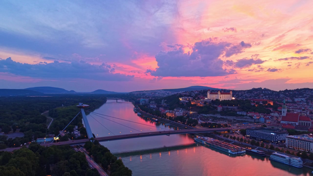 Solnedgang over floden i Bratislava. Solen går ned over floden i Bratislava, kaster farver hen over himlen og reflekteres i vandet.
