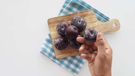 hand picking plums from a wooden cutting board