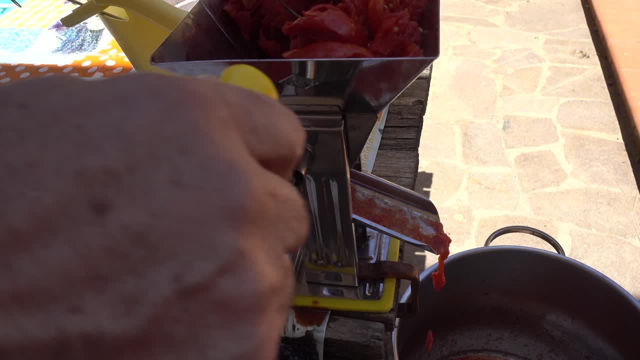 Preparazione della salsa di pomodoro. L'inquadratura mostra la salsa che esce dal lato destro della macchina mentre le bucce pressate vengono smaltite sul lato sinistro.