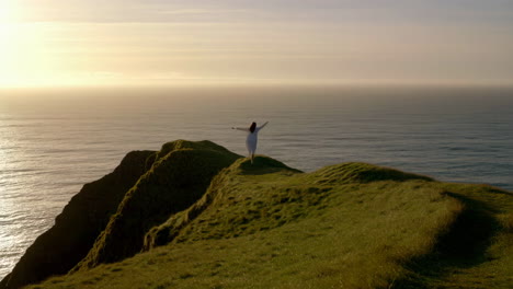 woman on a cliff overlooking the ocean at sunset