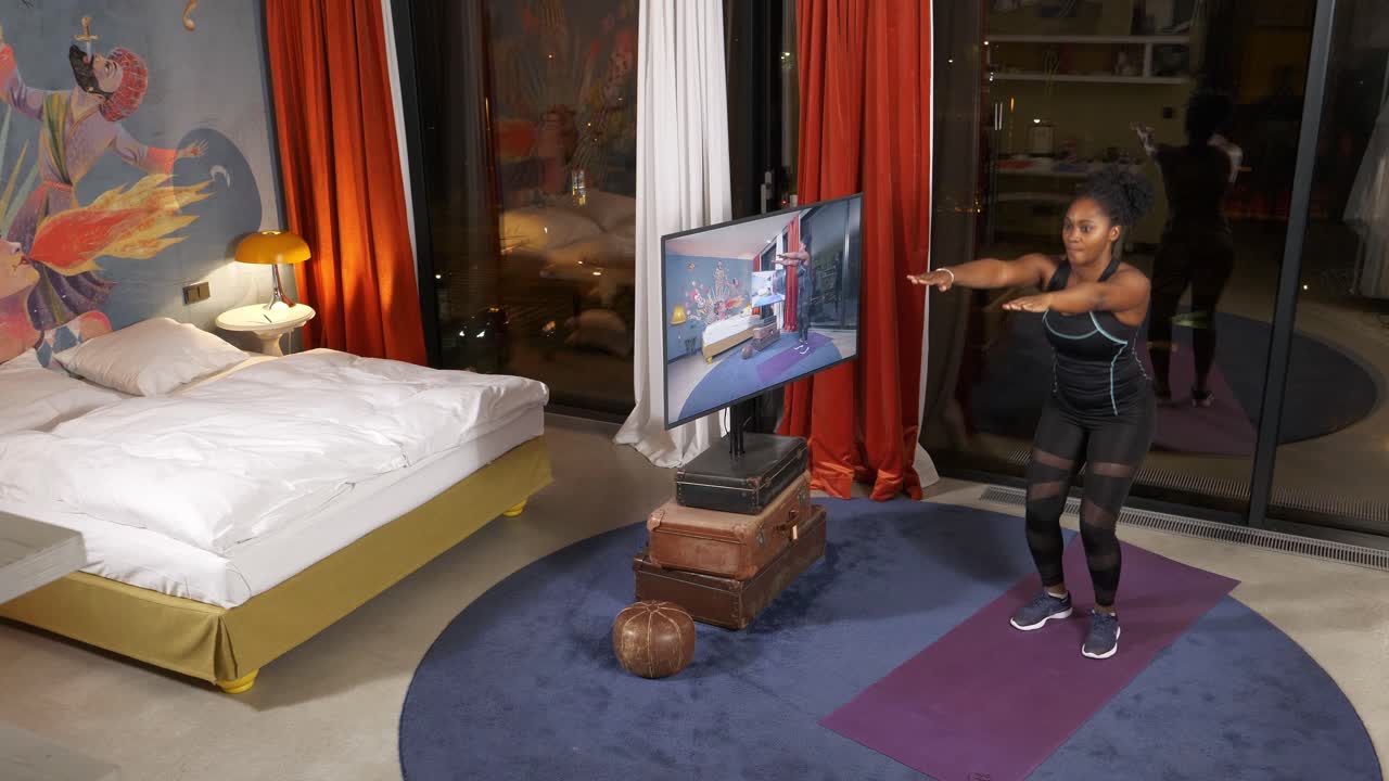 mujer haciendo una agachada después de un video de entrenamiento en un dormitorio elegante, por la noche