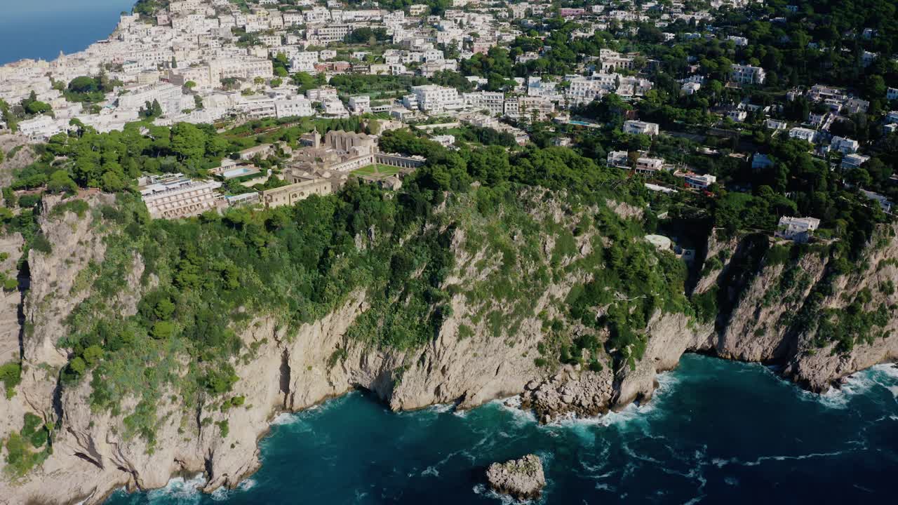 Vista aerea con drone che rivela la città dell'isola di Capri da un drammatico paesaggio di scogliere calcaree, bagnato dal Mar Mediterraneo turchese con grandi onde che si infrangono sulla costa rocciosa. Famosa destinazione turistica in Italia.