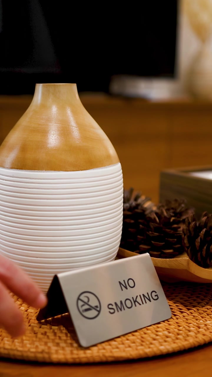A hand places a silver no smoking sign on a table beside an aromatherapy diffuser