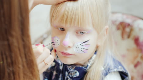 the child is applied with aquagrim tassel draws a cat mask concept - children's holiday