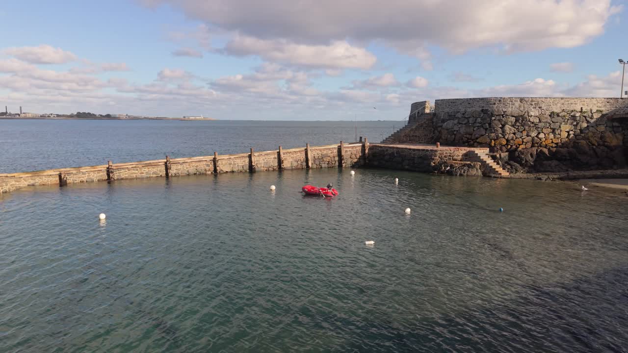 Filmato con panoramica lenta di Salerie Corner a St Peter Port Guernsey, con l'acqua che entra dolcemente nell'antico porto a metà marea, piccola barca all'ancora sotto il sole dorato con acqua limpida e calma e vista su St Sampson.