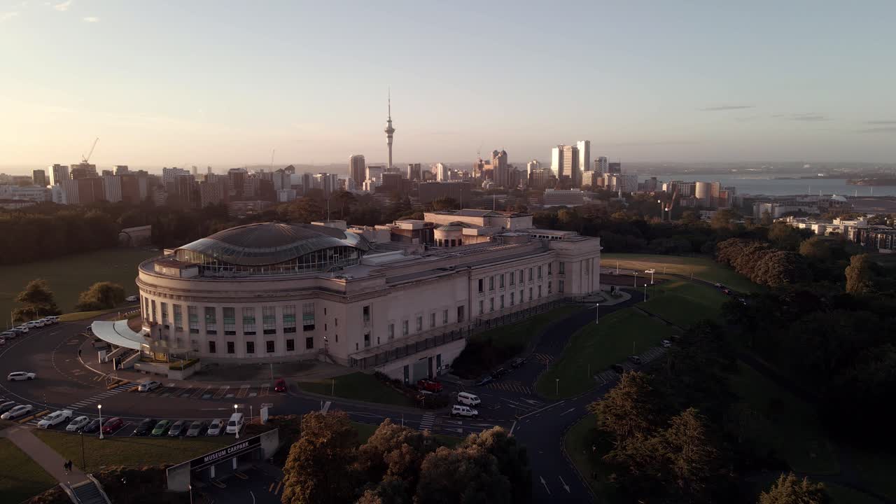 Circular aerial shot over Auckland Museum with skyline of Auckland city in the horizon at sunset