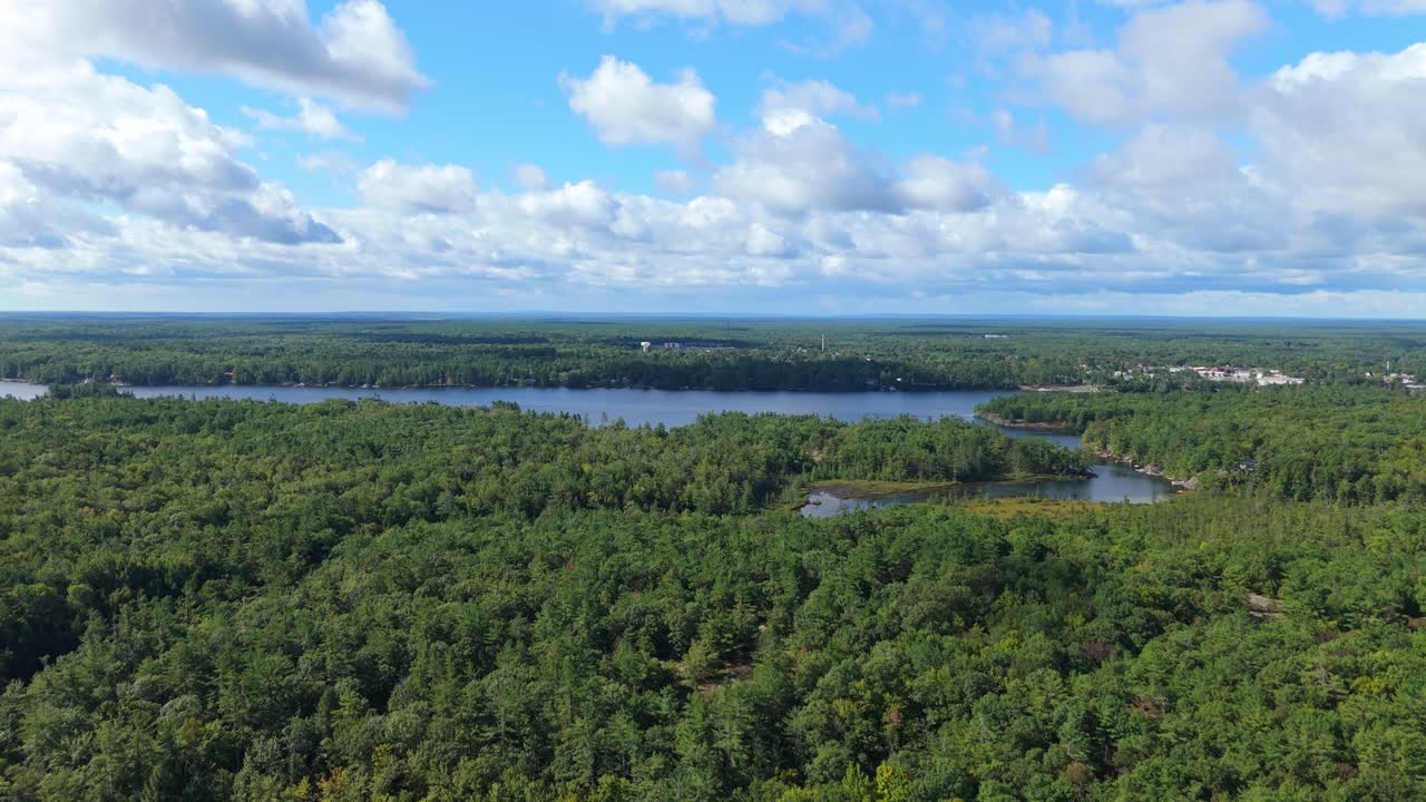 Drone high shot over Muskoka forest showing Gull Lake, clouds, and distant town