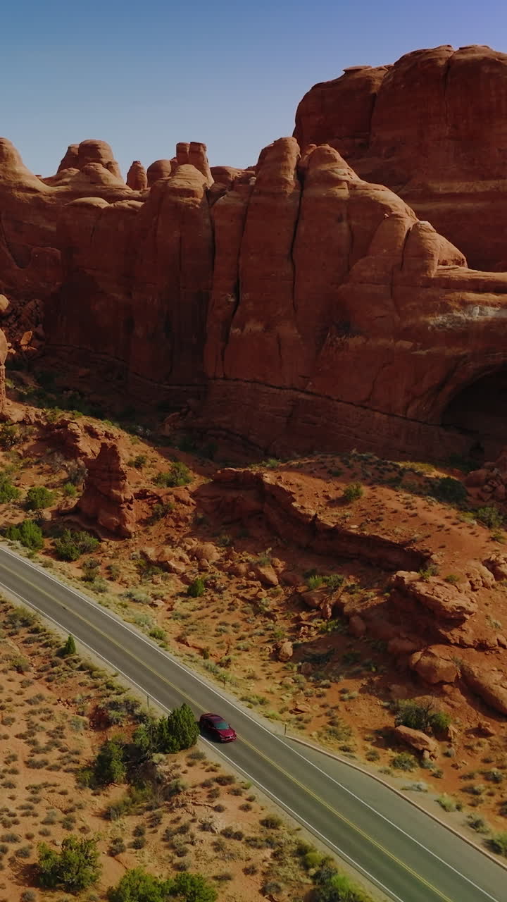 Cars moving by the motorway locating along the odd-shaped orange rocks. Wonderful canyons of Arches national park, Utah, USA. Vertical video