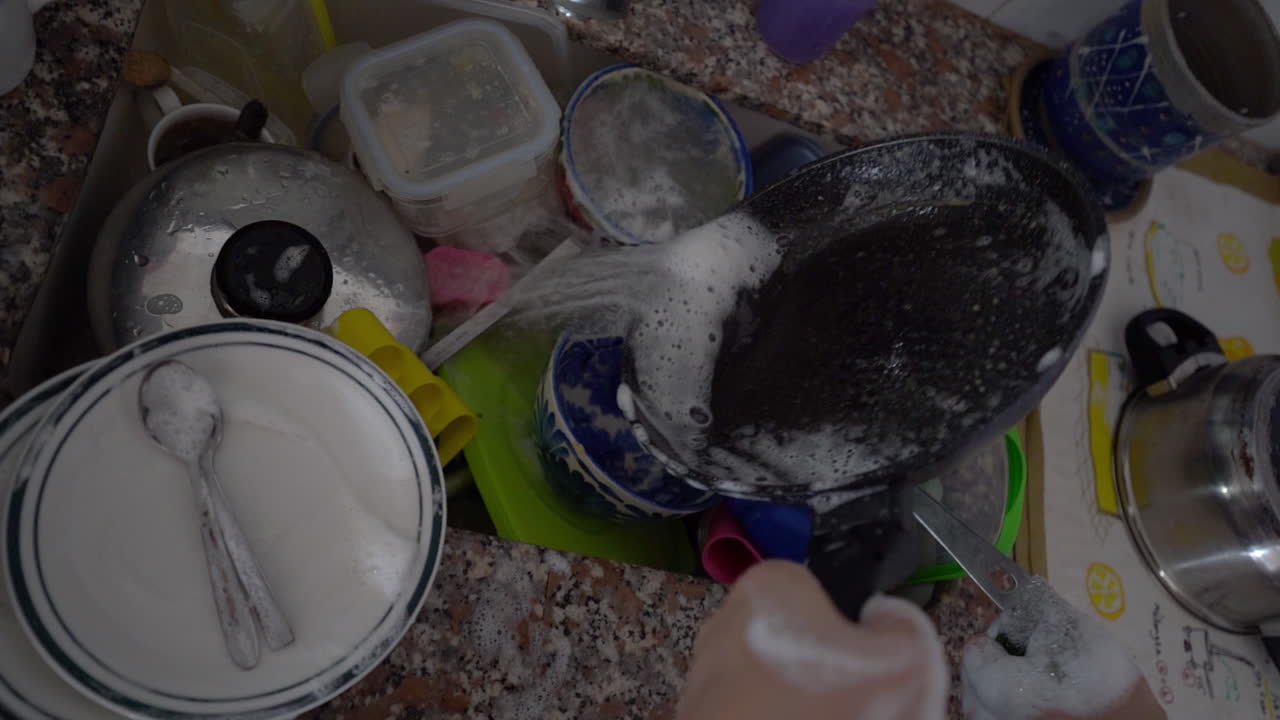 남자의 손은 더러운 접시로 가득 찬 싱크대에서 팬을 청소합니다