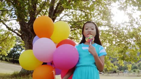 portrait of smiling girl holding balloons and lollypop in the park