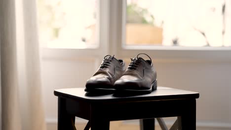 Men-brown-leather-shoes-set-on-a-stool-table-near-an-open-window,-Handheld-medium-shot