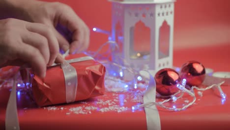 wrapping christmas gift with ribbon and red paper with red background and baubles