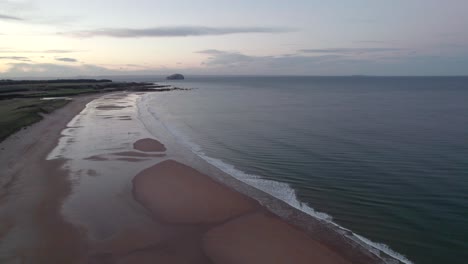 Drohnenaufnahmen,-Die-Langsam-Zu-Einem-Langen-Sandstrand-Hinabsteigen,-Während-Sich-Ein-Sonnenuntergang-In-Gezeitentümpeln-Widerspiegelt-Und-Die-Flut-Und-Die-Wellen-Sanft-Das-Ufer-Des-Strandes-Umspülen