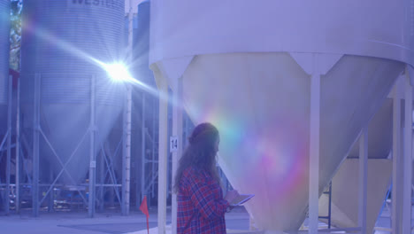 animación de luz brillante sobre una mujer caucásica con una computadora portátil trabajando en una fábrica