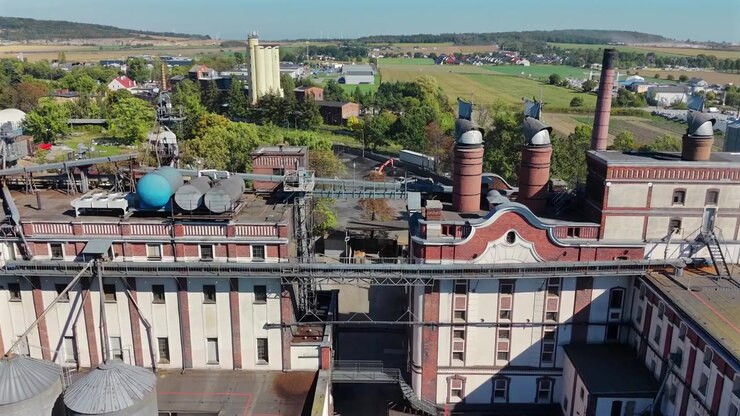 Ripresa aerea con drone del vecchio maltificio e degli edifici di maltazione a Strzegom con ciminiere in mattoni, silos per cereali e tetti, con campi e campagna sullo sfondo, Bassa Slesia, Polonia