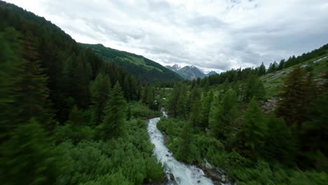 A-river-flowing-through-lush-green-valleys-with-mountains-in-the-background,-aerial-view