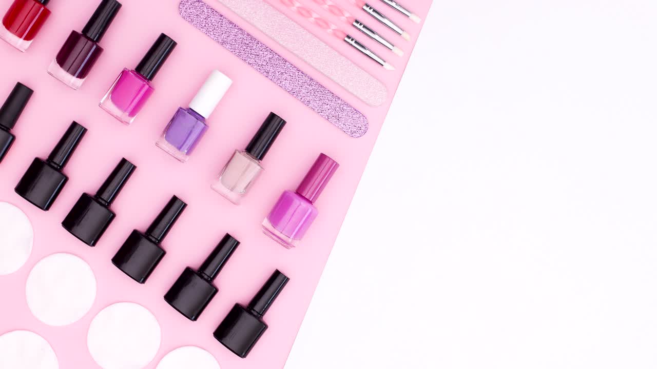 Nail polishes and manicure tools move on pink side of pink white theme. Stop motion