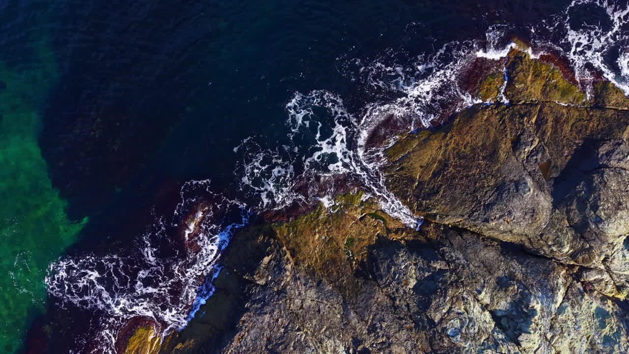 Waves dance upon rugged rocks at the shoreline during the golden hour near a tranquil coastal landscape