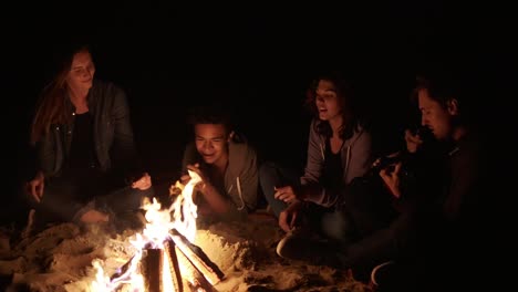 round camera movement: multiracial group of young boys and girls sitting by the bonfire late at night and singing songs and