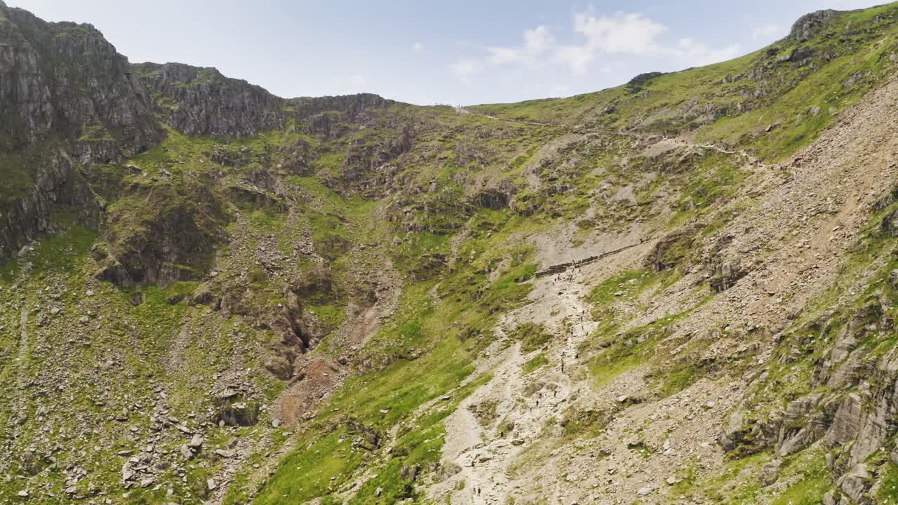 Smooth aerial descent past the cliff faces of Mount Snowden in Snowdonia National Park in Wales - Glacial landforms makes for challenging hiking trails for visiting adventurers and tourists