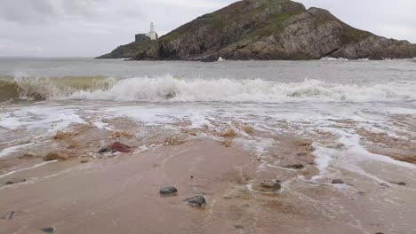 rough sea waves rolling in with island lighthouse background on windy day in mumbles swansea uk