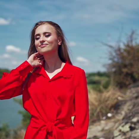 pretty woman in summer outdoors. beautiful girl with long hair on the river background. young model in red dress touching her hair and smiling. slow motion.