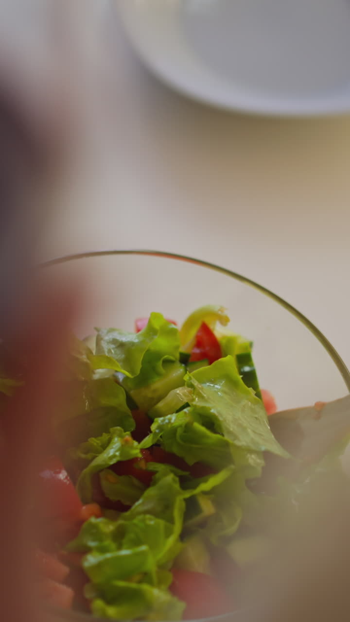 persona femenina agita ensalada fresca sosteniendo un vaso de vino tinto mientras hace la cena en la mesa en la cocina espaciosa en casa vista superior cercana movimiento lento