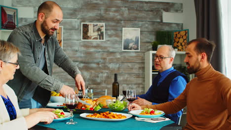 hombre sirviendo a un amigo con pollo asado en una cena familiar multigeneracional