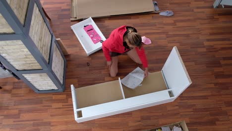 young girl looks over a half built table and then checks the instructions