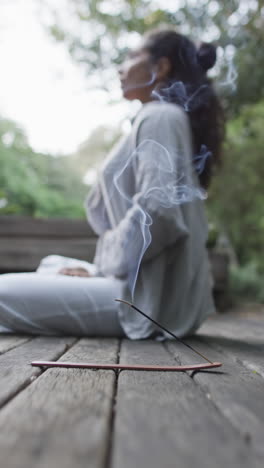 vertical video of focused biracial woman practicing yoga in sunny garden, slow motion