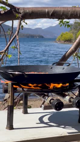 cooking paella on an outdoor stove with lago lacar in argentina as the backdrop