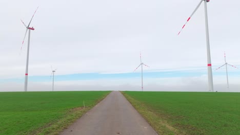 road through the wind farm with wind turbines over green field