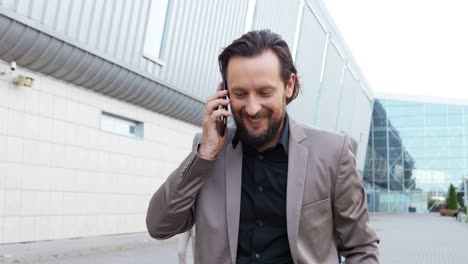 caucasian businessman in stylish clothes walking down the street and talking on the smartphone