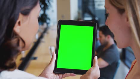cerca de dos mujeres de negocios mirando una tableta digital en blanco con pantalla verde en una oficina compartida