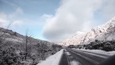 Road-trip-in-the-highlands,-Scotland,-snowy-road,-white-mountains-at-the-background,-traveling-shot