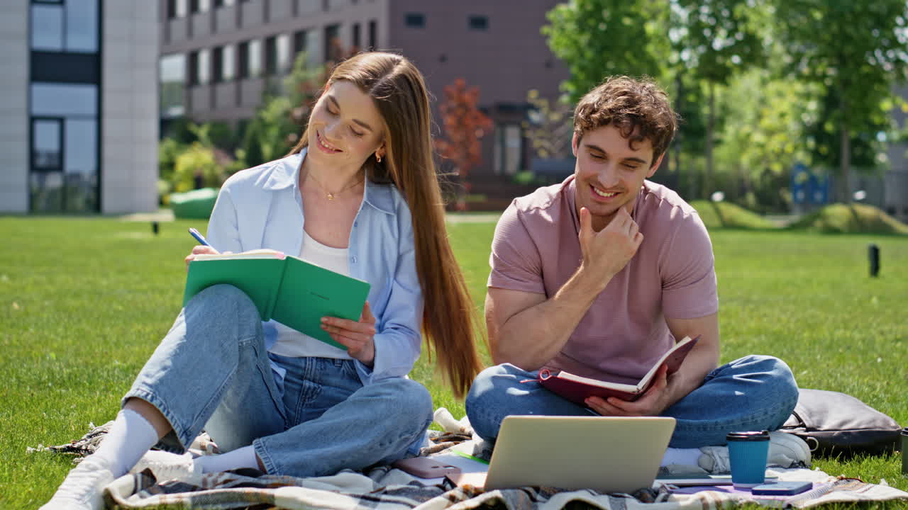 Focused couple working project together on green campus lawn. Young students