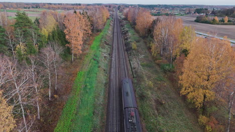 Birds-eye-drone-shot-of-country-fields-with-trees-and-highway-in-beautiful-fall-as-train-passes