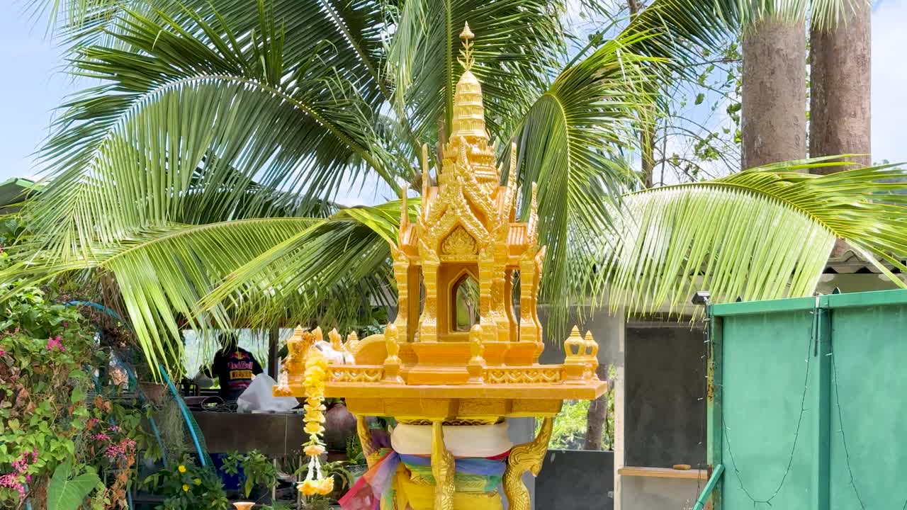 Golden shrine surrounded by lush greenery and palm trees under bright daylight in Phuket, Thailand