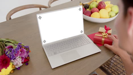 caucasian woman holding red gift using laptop with copy space on blank screen