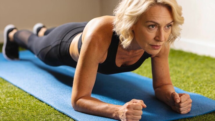 Donna in abbigliamento nero che mantiene la posizione del plank sugli avambracci su un tappetino blu a casa per la forza del core.