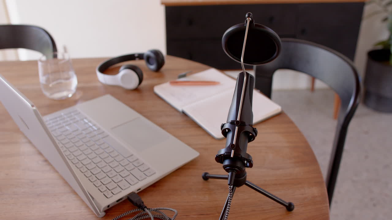 Podcasting setup with microphone, laptop, headphones, and notebook on wooden table