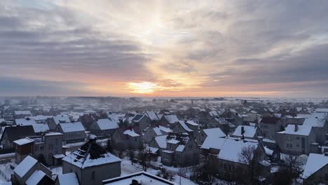 Panorámica-Aérea-De-Camiones-Con-Drones-De-Tejados-Cubiertos-De-Nieve-Y-Suburbio-De-Subdivisión-Con-Puesta-De-Sol-épica-Y-Nubes-Grises