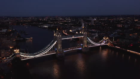 Slide-and-pan-footage-of-illuminated-Tower-Bridge.-Beautiful-old-tourist-attraction-at-night.-Cars-driving-across-River-Thames.-London,-UK