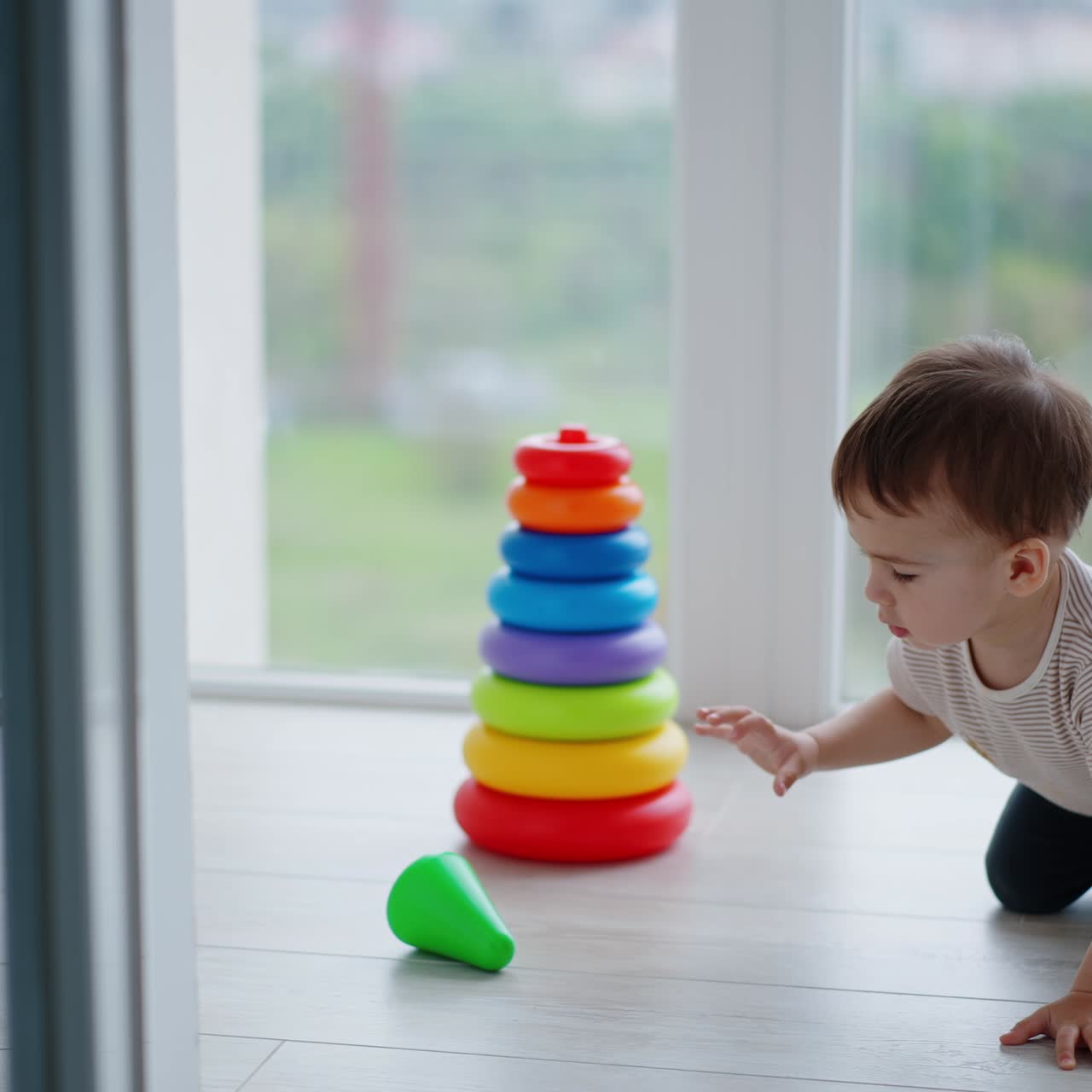 Baby boy assembled the colorful toy pyramid. Kid wants to take the top but distracts on something and moves back