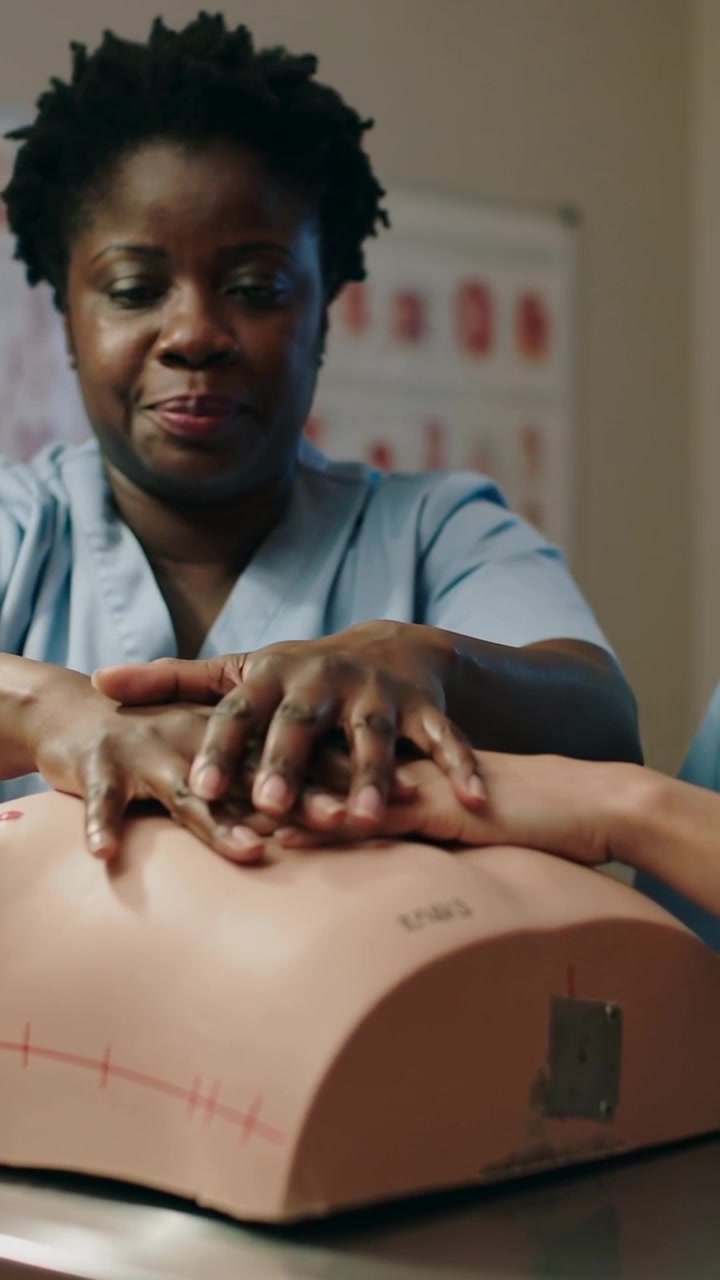 Vertical video: Placing hands, trainer in scrubs compressing manikin in sim lab for CPR training
