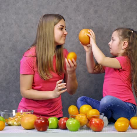 happy little girl and her mother with fruits at home. mother and daughter in pink t-shirts are having fun with fresh organic fruit in the kitchen.
