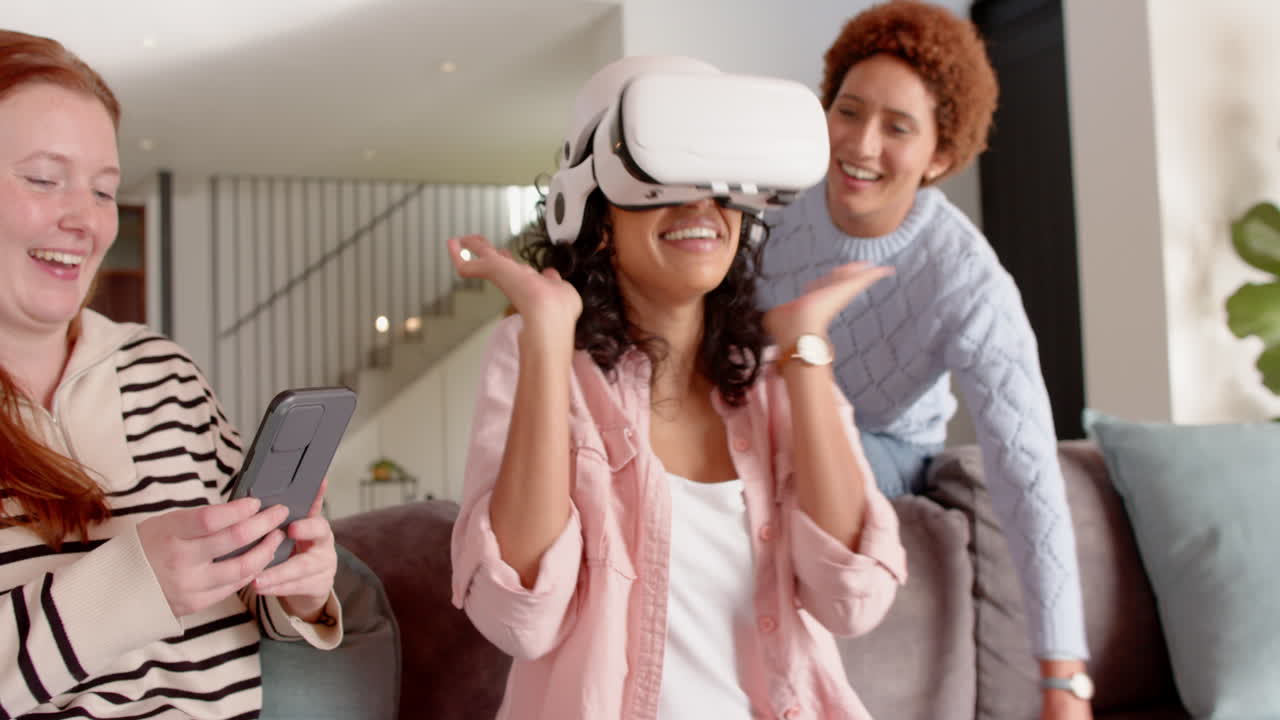 Donna che ride con le amiche, utilizzando un visore VR, tenendo in mano uno smartphone e godendosi il momento di svago.