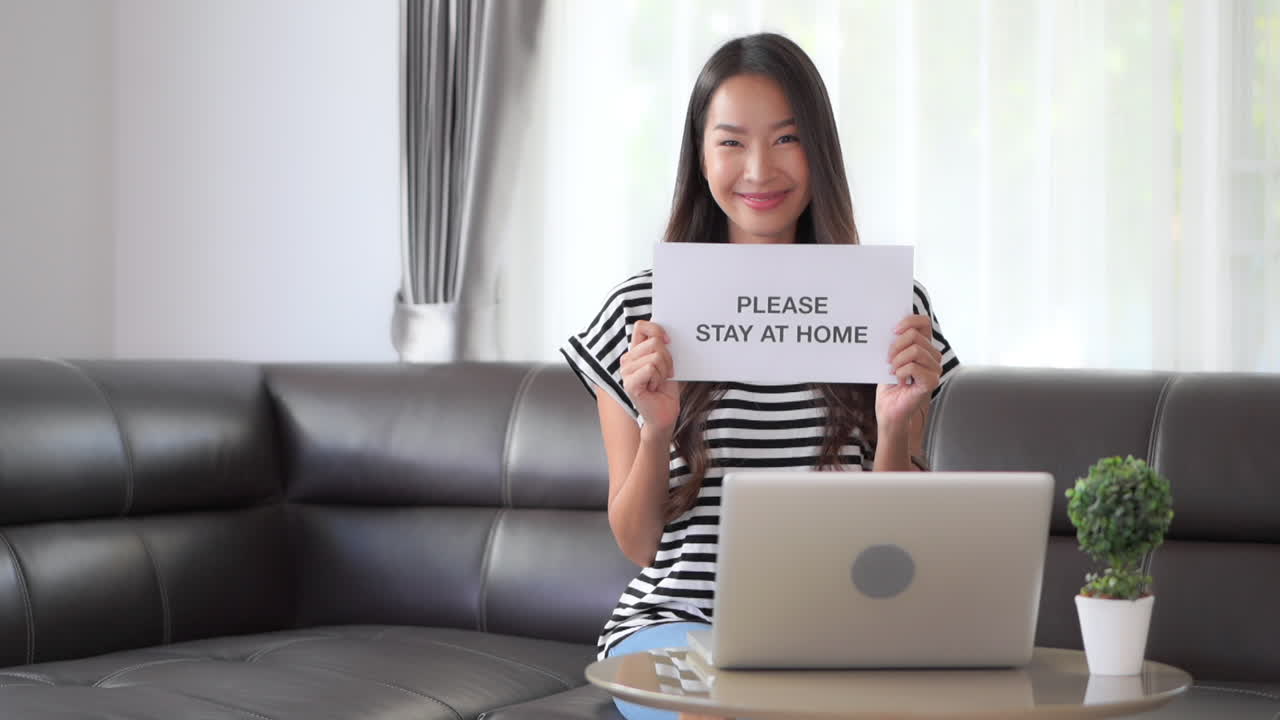 Social distancing, isolation, stay at home order related to Covid, coronavirus, pandemic. Smiling Asian model encouraging people to stay home by holding up sign Please Stay At Home