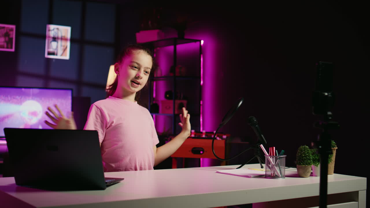 Bambina che intrattiene i follower, creando contenuti in un appartamento illuminato da neon rosa, usando il telefono su un treppiede.